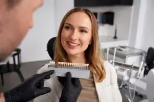 Close-up of a woman smiling while a dentist holds a veneer shade guide to match her teeth.